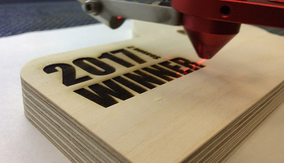 Laser engraving winner text onto birch ply award